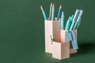 Cups with pens, pencils and stapler on green background