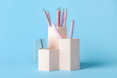 Cups with pens, pencils and stapler on blue background