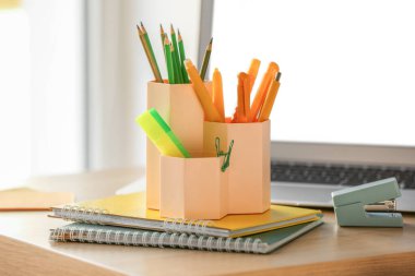 Cups with stationery and laptop on table in room, closeup