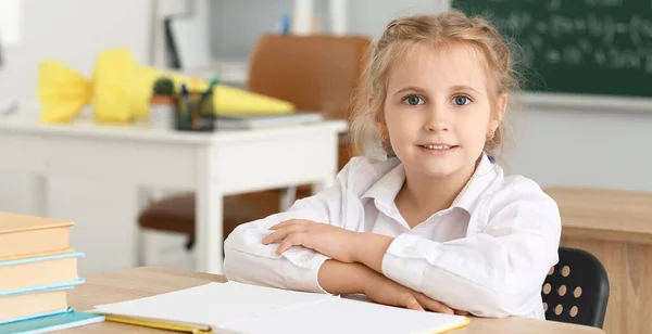 Cute little school girl sitting at desk in classroom