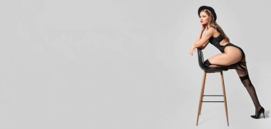 Fashionable young woman in underwear and stockings near chair on grey background with space for text