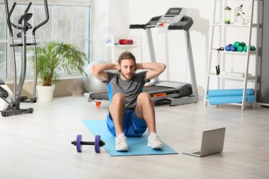 Sporty young man with laptop training in gym