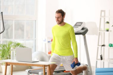 Sporty young man using laptop for online training in gym