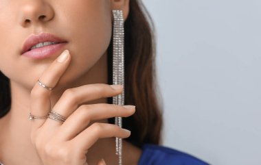 Beautiful young woman with stylish jewelry on light background, closeup