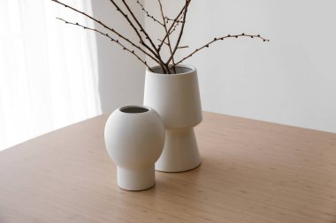 Vases with branches on wooden table in room