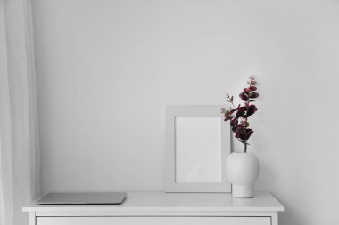 Vase with eucalyptus branches, laptop and photo frame on table in light room