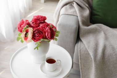 Vase with bouquet of beautiful flowers and cup of coffee on table in room