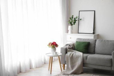 Interior of light room with sofa, table and chest of drawers near window