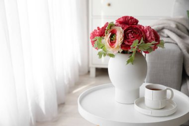 Vase with bouquet of beautiful flowers and cup of coffee on table in room