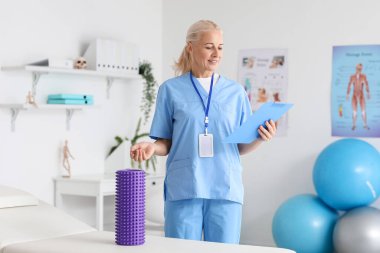 Mature physiotherapist with clipboard and foam roller in rehabilitation center