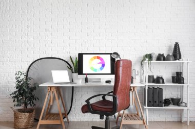 Photographer's workplace and shelving unit with equipment near white brick wall in studio