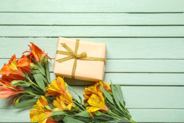 Beautiful alstroemeria flowers and gift box on color wooden background