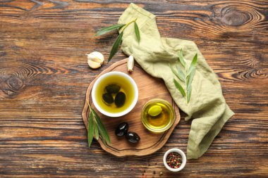Composition with bowls of fresh oil, olives and spices on wooden background