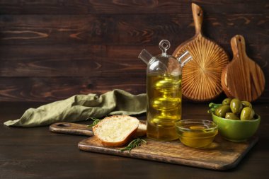 Board with bottle of fresh oil, bread and olives on dark wooden background
