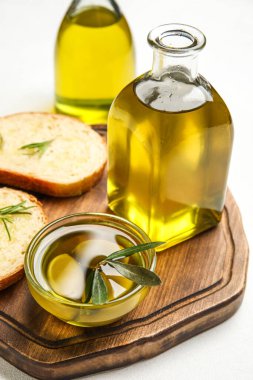 Wooden board with bottle of fresh olive oil, olives and bread on light background, closeup