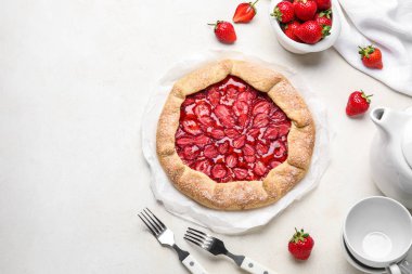 Composition with tasty strawberry galette, fresh berries and cups on light background
