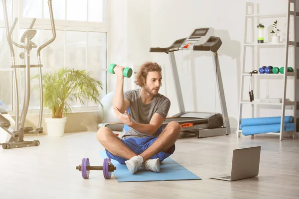 Sporty young man with laptop training in gym