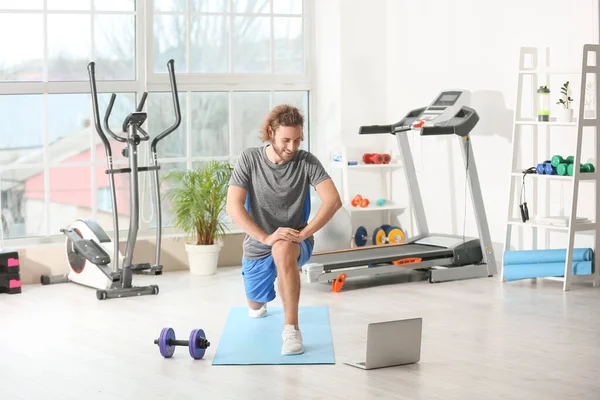 Sporty young man with laptop training in gym