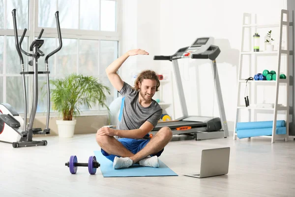 Sporty young man with laptop training in gym