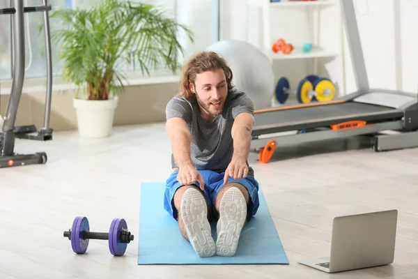 Sporty young man with laptop training in gym