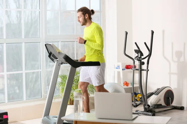 Sporty young man using laptop for online training in gym