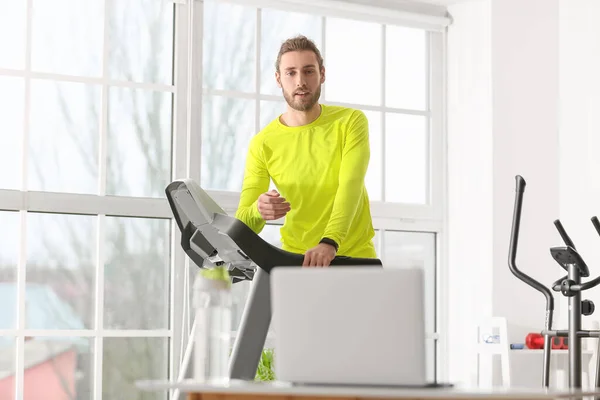Sporty young man using laptop for online training in gym