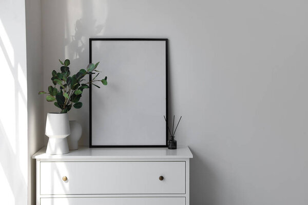 Chest of drawers with vases and photo frame in light room