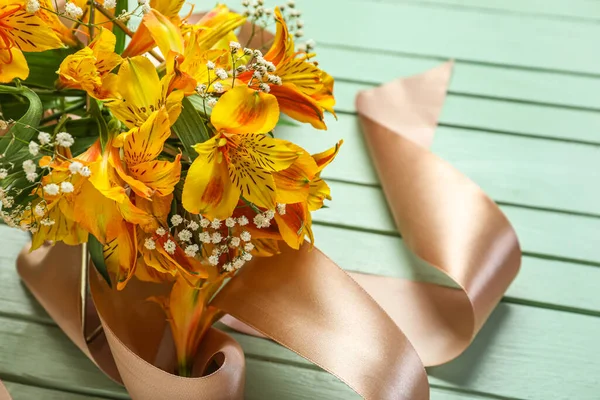 Beautiful alstroemeria flowers and ribbon on color wooden background, closeup