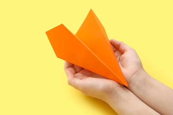 Woman with orange paper plane on yellow background, closeup