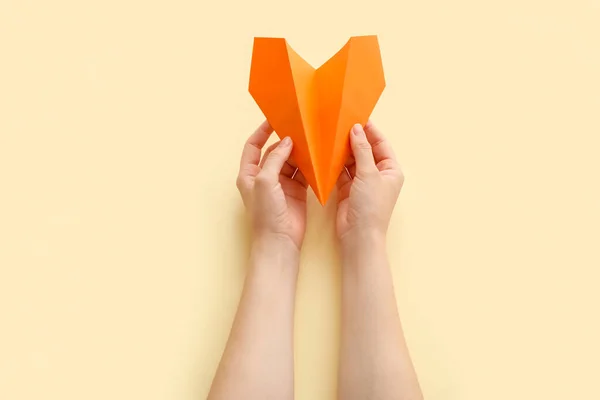 Woman with orange paper plane on beige background