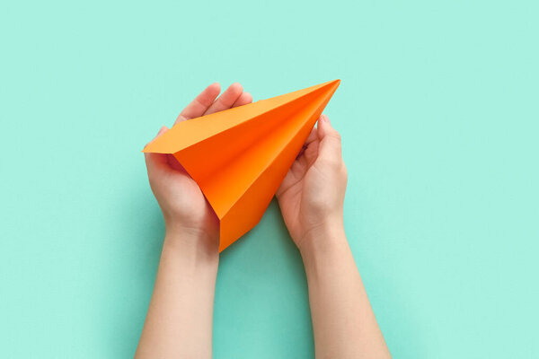 Woman with orange paper plane on color background