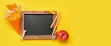 School cone, chalkboard, apple and stationery on yellow background with space for text, top view
