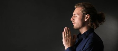Religious young man praying on dark background with space for text