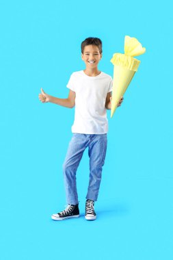 Little boy with yellow school cone showing thumb-up on blue background