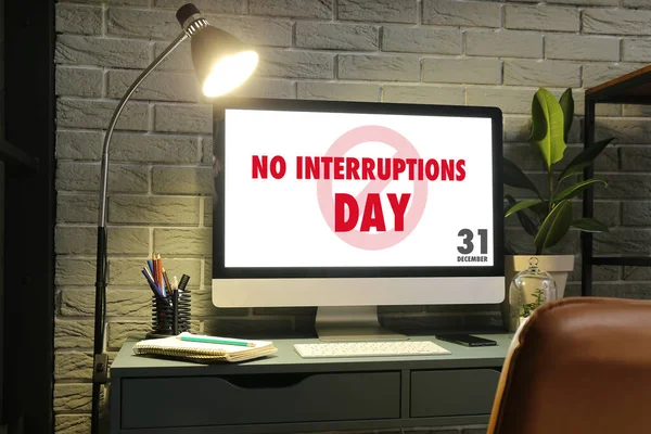 Text NO INTERRUPTIONS DAY on screen of computer monitor at workplace in office late in evening