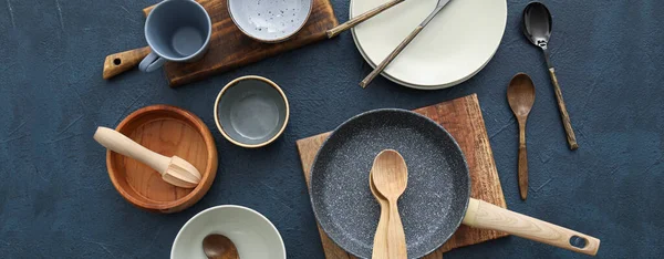 Set of kitchen utensils and dinnerware on dark background, top view