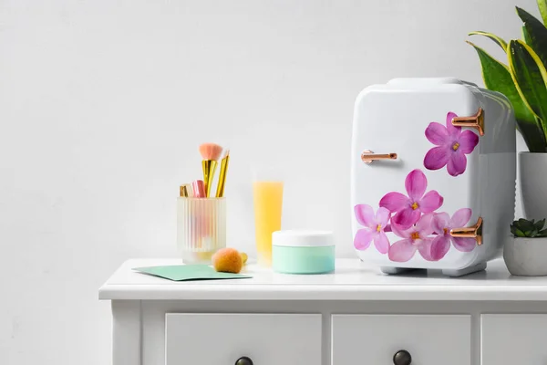 Small refrigerator with floral print and cosmetic products on table in room