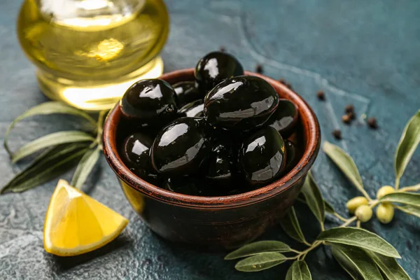 Bowl of tasty black olives on dark color background, closeup