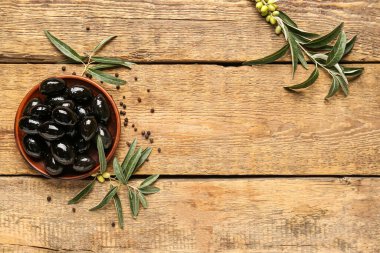 Composition with plate of tasty black olives, tree branches and peppercorns on wooden background