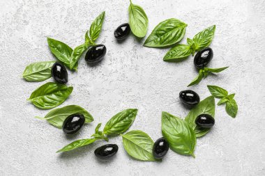 Frame made of tasty black olives and basil on light background