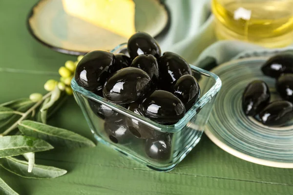 Glass bowl of tasty black olives on color wooden background