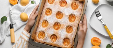 Hands holding baking tray with tasty apricot pie on light background, top view