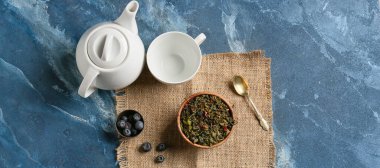 Composition with dry tea leaves, cup, teapot and blueberry on color background