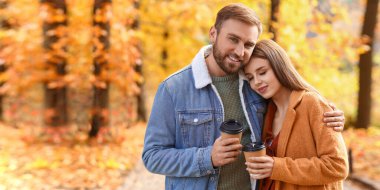 Happy young couple with cups of coffee in autumn park