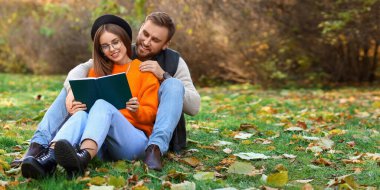 Happy young couple reading book together in autumn park