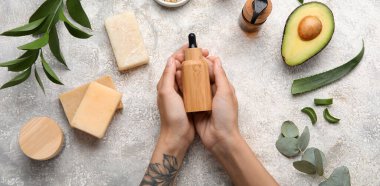 Female hands with bottle of essential oil, soap and natural ingredients on light background, top view