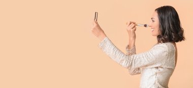 Beautiful young woman applying makeup on beige background with space for text