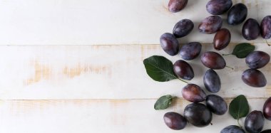 Many plums on white wooden background with space for text, top view
