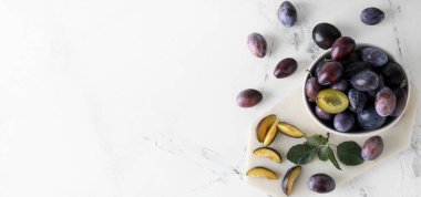 Bowl of tasty plums on light background with space for text
