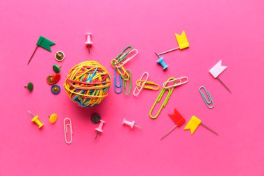 Composition with ball of colorful rubber bands, paper clips and pins on pink background